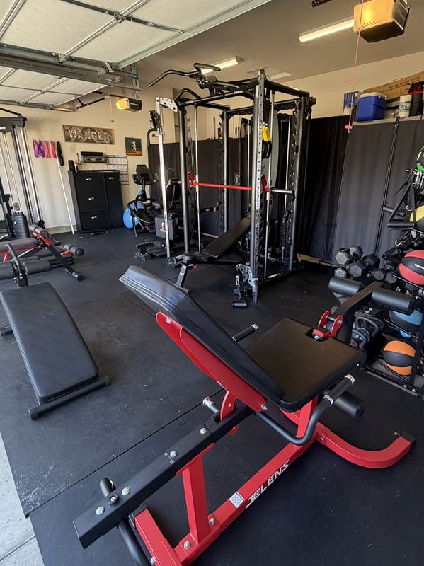 Red preacher bench in the foreground with the power rack and dumbbells behind